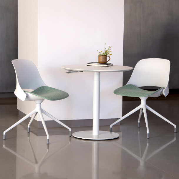 Two modern Humanscale Trea chairs with green seats and white frames around a Humanscale Float Gather 30" round table in a minimalistic setting. Kansas City Office Design.