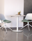 Two modern Humanscale Trea chairs with green seats and white frames around a Humanscale Float Gather 30" round table in a minimalistic setting. Kansas City Office Design.