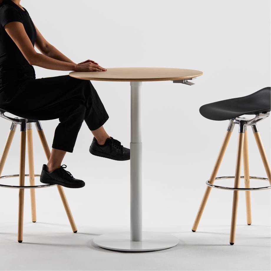 Person sitting at a Humanscale Float Gather table with black stools on a white background. Kansas City Office Design.
