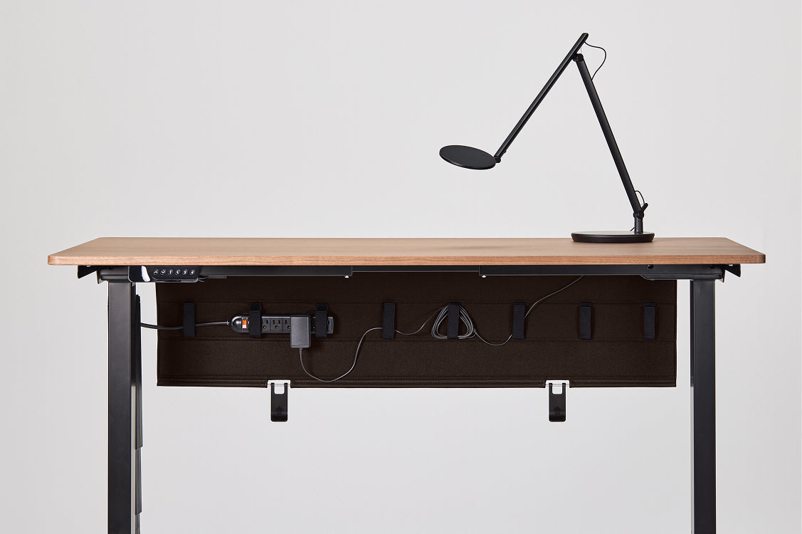 Wooden desk with black metal frame and a lamp on a white background. This includes the Humanscale NeatTech Cable Management tray installed under the surface. Kansas City Office Furniture.
