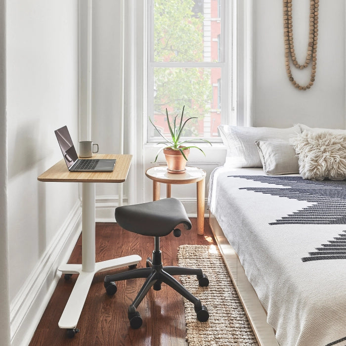 Small home office with a Humanscale Float Mini standing desk, Humanscale saddle chair, and laptop in a bedroom setting. Kansas City Office Design.