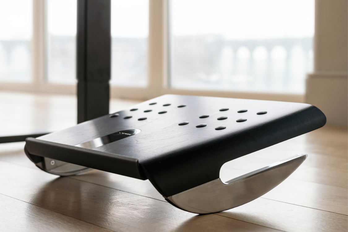 Humanscale black footrest on a wooden floor with large windows in the background. Kansas City Office Design. 