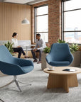 Modern office waiting area with blue chairs, a wooden table, and people sitting. Kansas City Office Design.