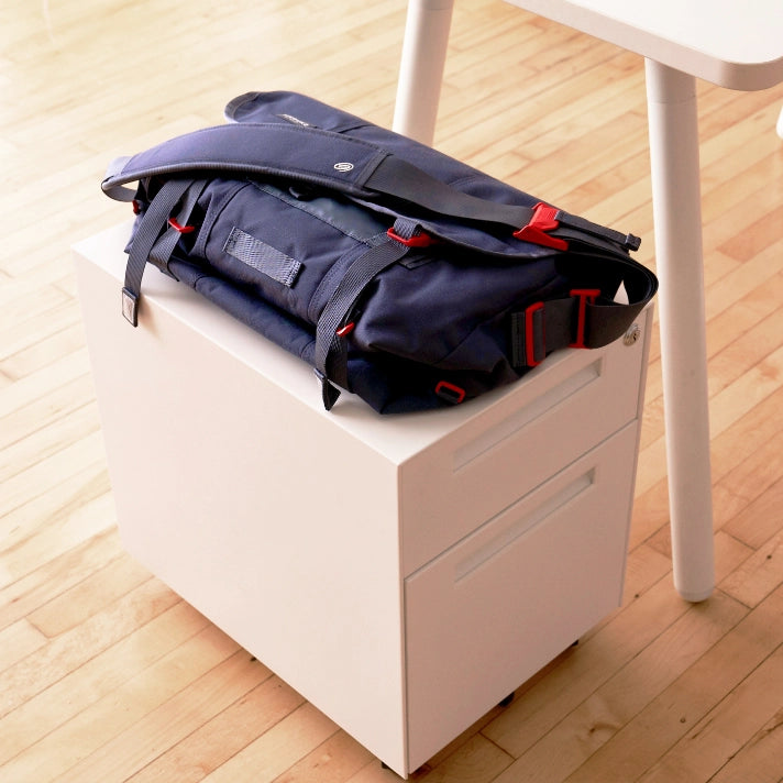 Black bag with red accents on a white mobile storage pedestal under a white table. Kansas City Office Furniture.