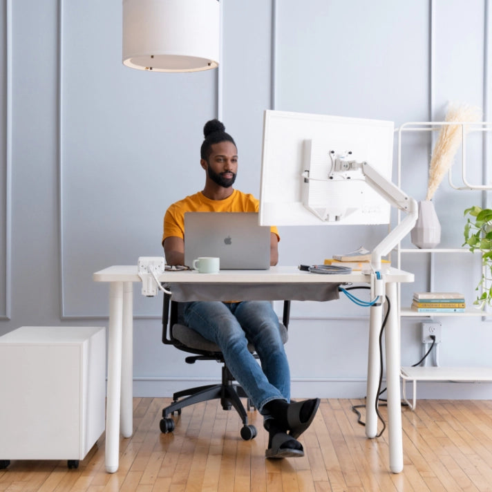 Person sitting at a desk with a laptop and computer monitor in a modern office setting. Kansas City Office Design.