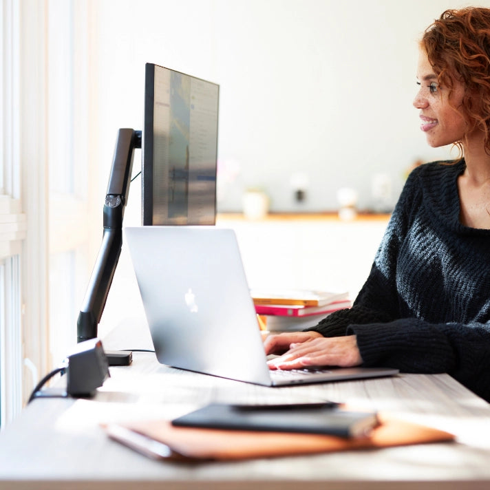 Woman working at a desk with a laptop and monitor in a home office setting. Kansas City Office Design.