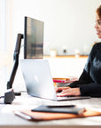 Woman working at a desk with a laptop and monitor in a home office setting. Kansas City Office Design.