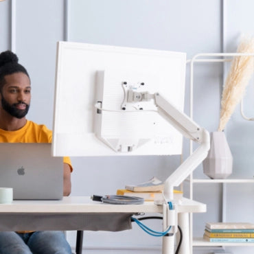 Person using a laptop with a white adjustable SitOnIt Mobio monitor stand in a home office setting. Kansas City Office Design.