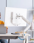 Person using a laptop with a white adjustable SitOnIt Mobio monitor stand in a home office setting. Kansas City Office Design.
