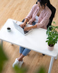 Person sitting at a white SitOnIt Reya desk using a laptop with a plant and cup of coffee on the desk. Kansas City Office Design.