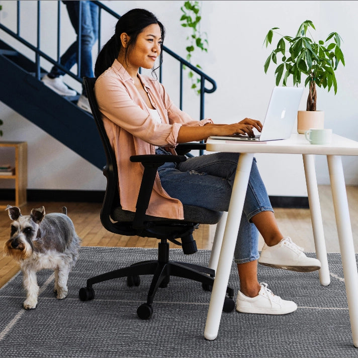 Woman working on a laptop at a SitOnIt Reya desk with a small dog nearby. Kansas City Office Design.