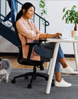 Woman working on a laptop at a SitOnIt Reya desk with a small dog nearby. Kansas City Office Design.