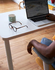 Person sitting at a SitOnIt Reya desk with a laptop, mug, and glasses on a wooden floor. Kansas City Office Design.