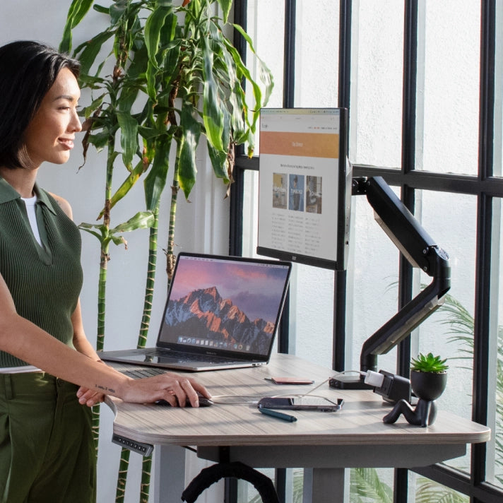 Woman using a laptop at a standing desk with a plant in the background. Kansas City Office Design.