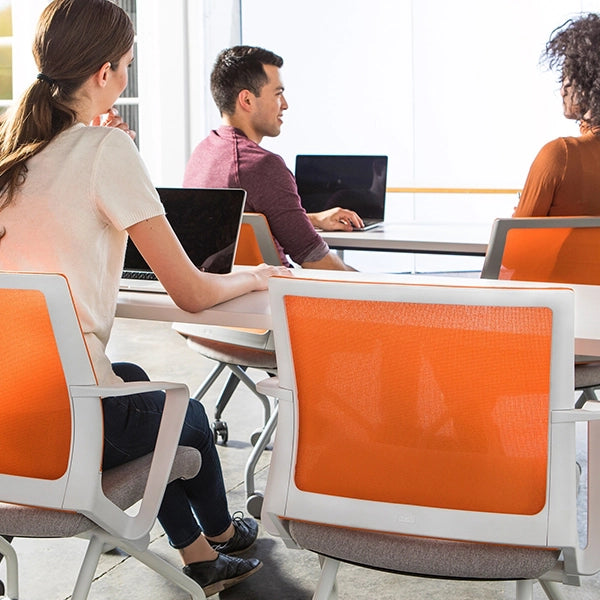 Three people working on laptops in a modern office setting with orange chairs. Kansas City Office Design.