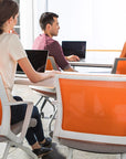 Three people working on laptops in a modern office setting with orange chairs. Kansas City Office Design.