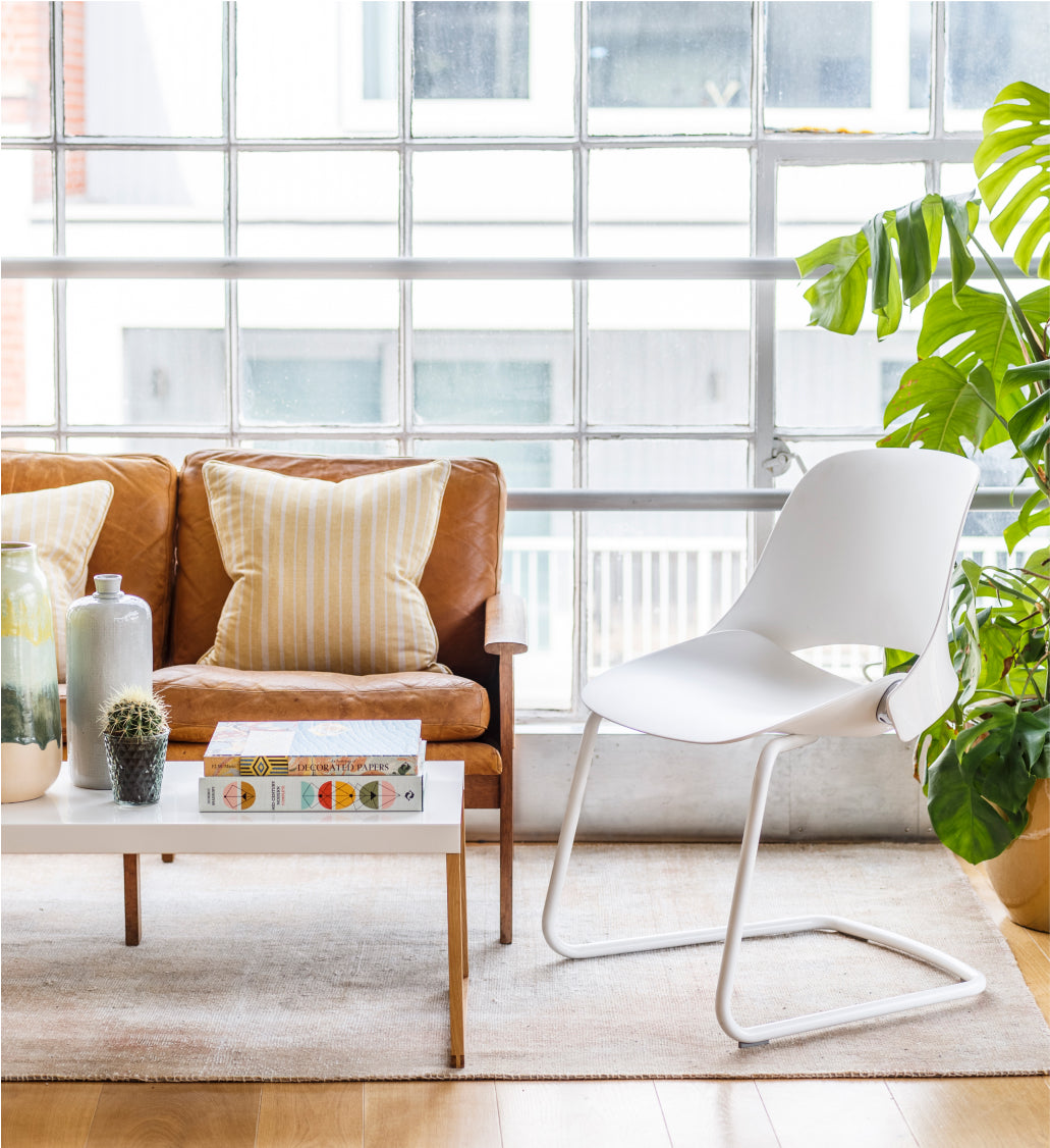 Humanscale Trea Cantilever Base Chair. Modern living room with a brown sofa, white chair, and coffee table. Kansas City Office Furniture. 
