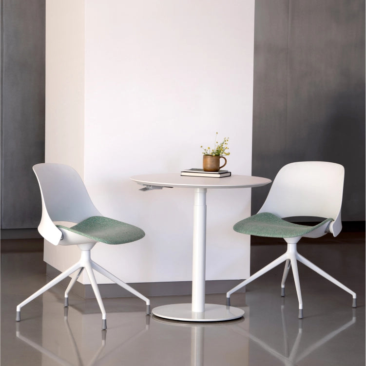 Modern white chairs with green seats around a small round table in a minimalistic setting. Kansas City Office Design