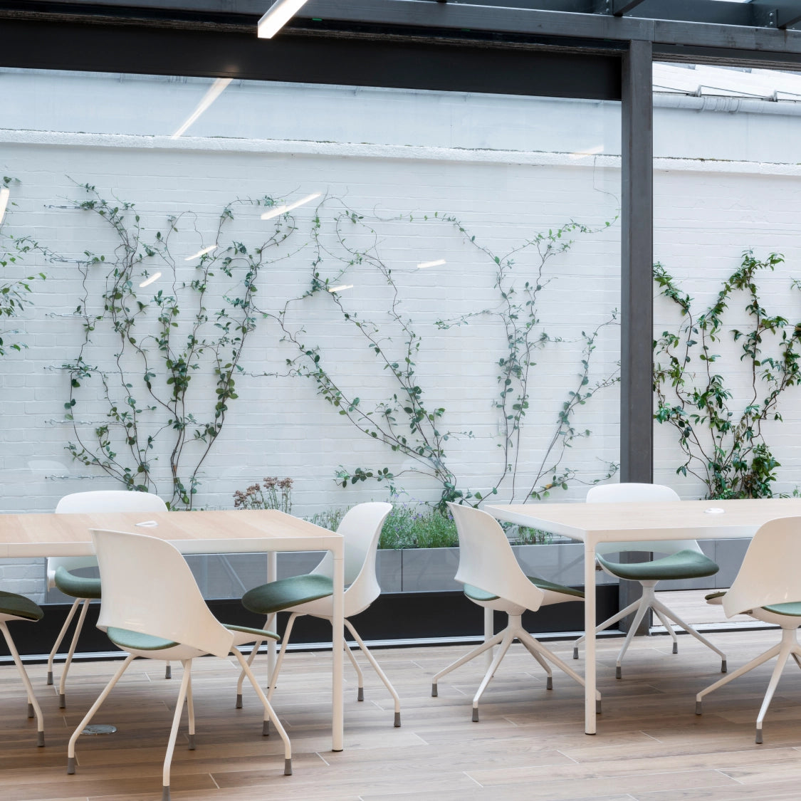 Modern office setting with white tables and chairs against a white brick wall with greenery. Kansas City Office Design