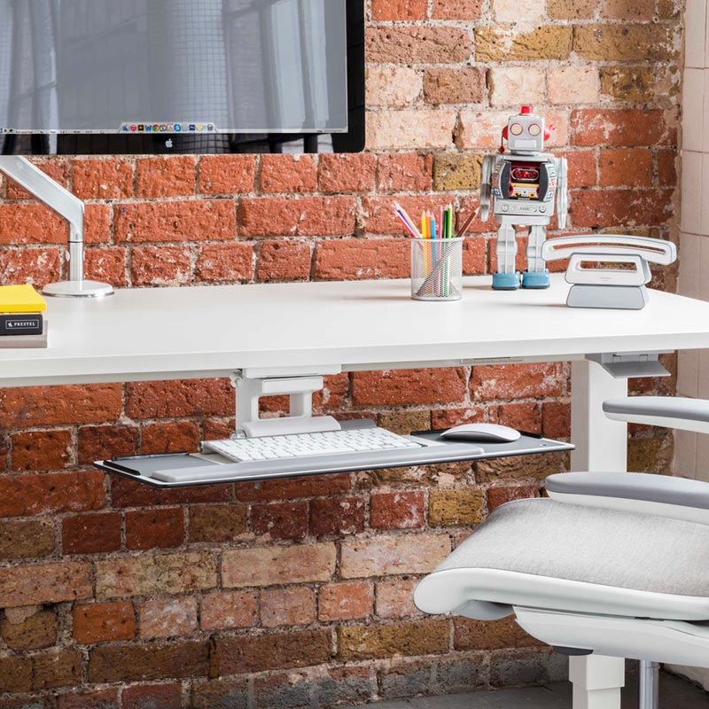 HumanScale keyboard tray meant for height adjustable desk. Pictured with a desk, chair, monitor against a brick wall. Kansas City Office Design.